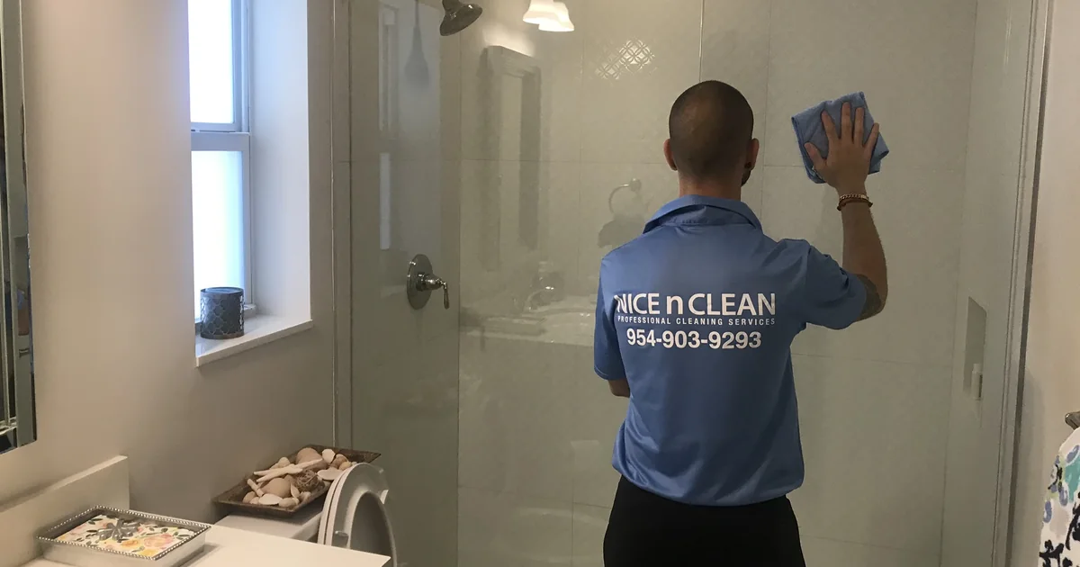 A NiceNClean cleaner wiping a glass shower door in a Fort Lauderdale bathroom